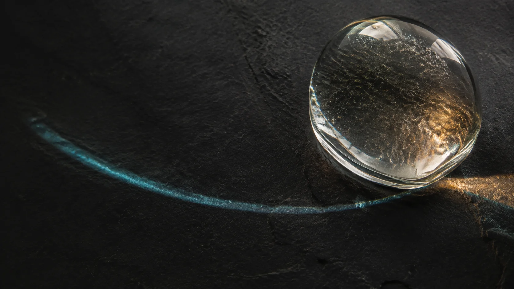 Sculptural glass refracting cyan and amber light across dark stone